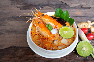Tom Yum Goong or Shrimp soup spicy sour Soup Traditional food in Thailand contains chili, lime,lemongrass, lime leaf, along with cooked rice in a white dish on the old wood background.