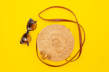 Obraz premium Top view female summer fashion straw round bag and sunglasses on a yellow table background