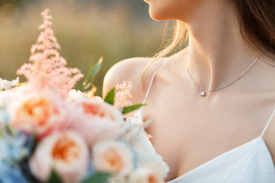 Bride at sunset holding a wedding bouquet in her hands. Beautiful collarbone and pendant