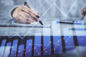 Double exposure of woman's hands making notes with forex graph hologram. Concept technical analysis.