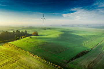Wind turbine on foggy green field at sunrise