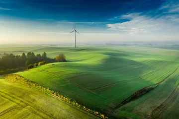 Wandaufkleber Windkraftanlage auf nebliger grüner Wiese bei Sonnenaufgang © shaiith