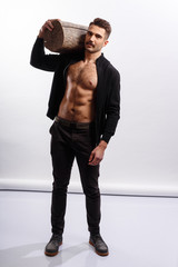Strong brutal man with haircut, with naked torso, holding a wooden log on his shoulders, looks at camera on a white background.