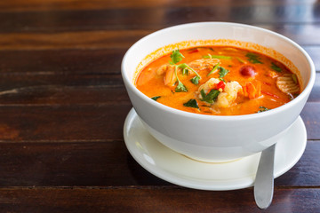 Tom Yam kung Spicy Thai soup with shrimp in white bowl on wood table. With copy space for text or...