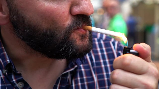 Young man lighting up cigarette with lighter in the city, slow motion