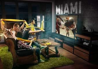 Group of friends watching TV, american football match, championship. Emotional men and women cheering for favourite team, look on fighting for ball. Concept of friendship, sport, competition, emotions