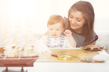 Happy kid and mom playing with toy sailing boat indoors. Travel and adventure concept