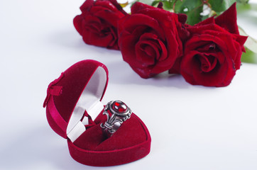 Signet with a stone in a gift box, two red hearts and a bouquet of red roses. On a white background.