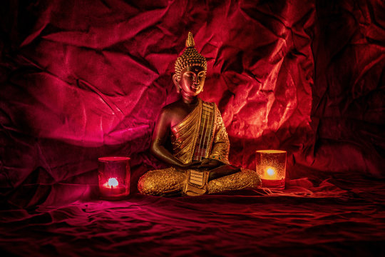 A golden buddha statue on red velvet with two candlelights