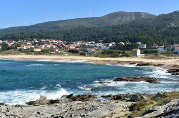 Fototapeta premium Small coastal village with wild beach, forest and hill. View from the rocks with blue sky. Galicia, Spain.