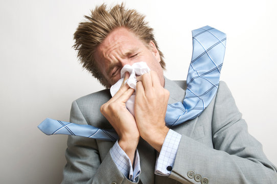 Sick businessman blowing his nose with enough pressure to send his tie flying