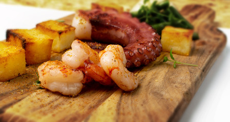 Grilled octopus tentacle on a wooden cut board served with shrimps