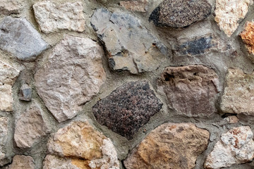 The wall of natural stone of gray and brown is laid out in the form of bricks with cement. Building from ecological material, construction background from rock texture close-up.