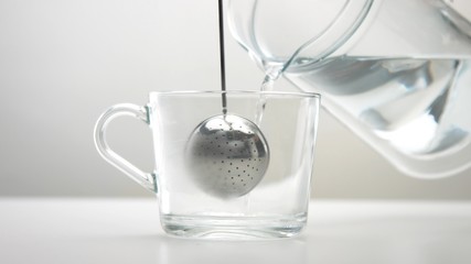 Closeup of transparent cup with brewed tea and a infuser tea spoon Clear hot water pouring into the cup