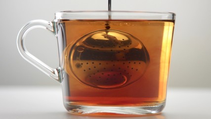 Closeup of transparent cup with brewed tea and a infuser tea spoon. Tea ceremony concept