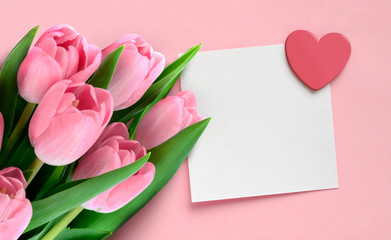 Fototapeta premium Valentine Mother's day greeting card with pink tulips and blank paper note with heart on pink background.