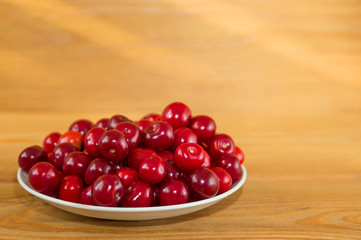 Ripe red cherries on a wooden background. Red berries on a plate on a brown background.