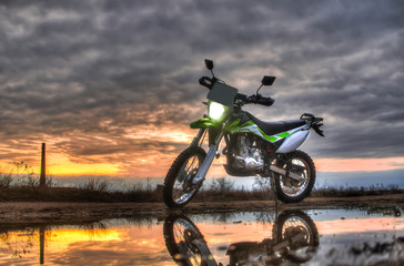 Beautiful green off-road motorcycle Enduro or cross, in reflection in a puddle on the background of sunset and sky HDR