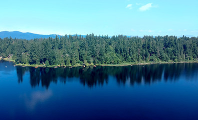 Fototapeta premium Photogenic Spring Lake on a bright clear day in summertime with trees reflecting in the water a blue sky and white clouds with lily pads dockside in Renton King County Washington State