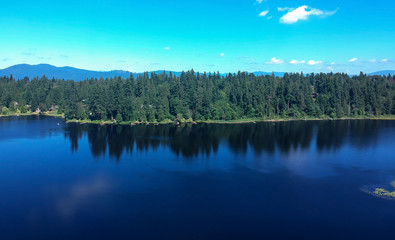 Fototapeta premium Photogenic Spring Lake on a bright clear day in summertime with trees reflecting in the water a blue sky and white clouds with lily pads dockside in Renton King County Washington State