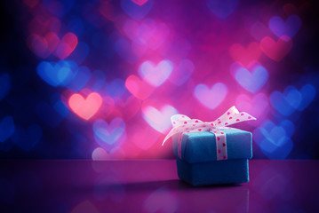 Blue gift box over heart shaped holiday defocused lights. Valentines day concept