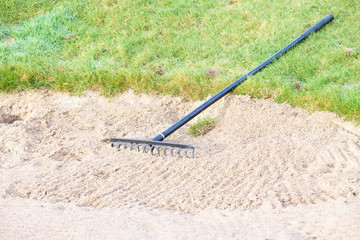 Rake in sand bunker at golf links course green for golfers