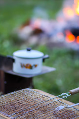 Meat on the grill and white pan on the brazier on bonfire background