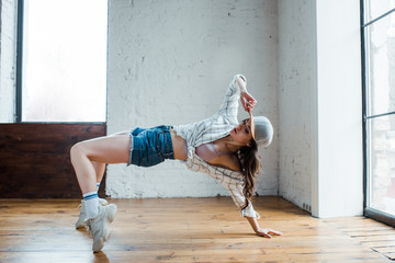 attractive girl touching cap while dancing hip-hop in dance studio