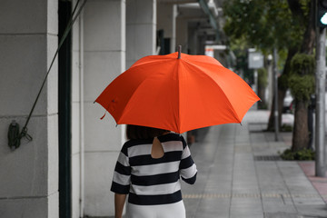 Back view of woman with orange umbrella walking on a street.