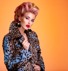 Beautiful woman with style hairstyle. White woman with bright colored makeup. Fashionable young woman is in the spotted fur coat. Stunning blonde girl. Bright eye makeup. Attractive sexy model poses