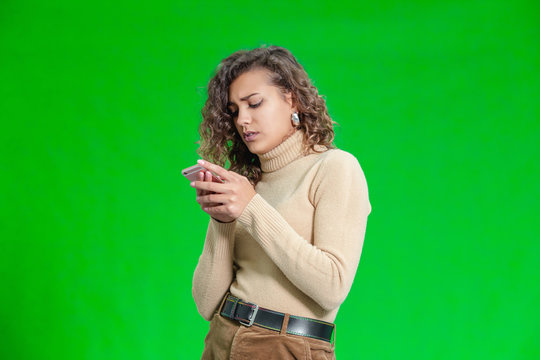 Portrait of anxious and puzzled girl looking at smartphone screen, being worried, standing over gren background.