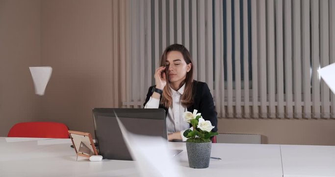 Girl clerk was tired of constant monotonous work and threw sheets of paper into air, indifference and fatigue, beautiful girl in office, sitting at her laptop, sent job to hell, felt relieved, smiled