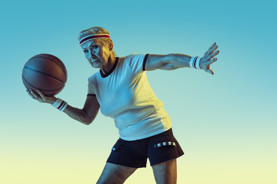 Senior woman in sportwear playing basketball on gradient background, neon light. Female model in great shape stays active. Concept of sport, activity, movement, wellbeing, confidence. Copyspace.