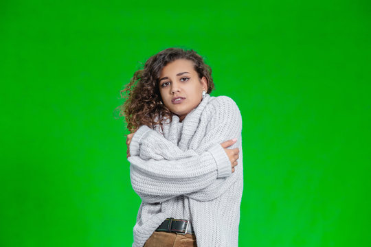 Pretty female covering herself in a warm sweater, but it is still cold and she is trembling.