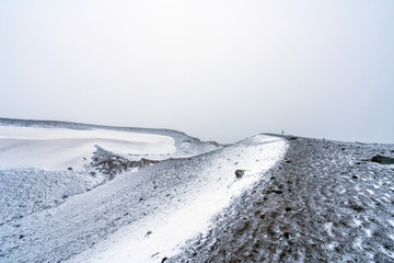 Girl with blue jacket stands on top of a volcano in geothermal and volcanic area near Krafla in Iceland..Foggy and snow covered ashy landscape. Explore and traveling concept.