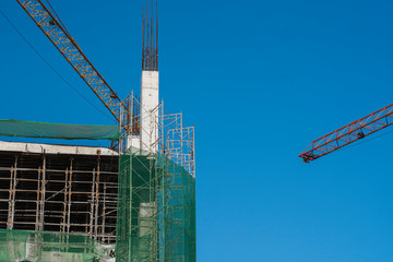 Cranes and building construction site against blue sky. Metal construction of unfinished building...
