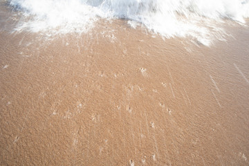 The red sandy beach is covered with white wave bubbles above in the evening.