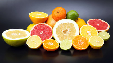 cut pieces of different citrus fruits on dark background