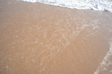The red sandy beach is covered with white wave bubbles above in the evening.