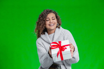 Fototapeta premium Christmas woman holding Christmas gifts in her arms wearing warm woolen sweater isolated on green background.
