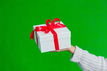 Close up of female hand holding white gift box tied with red ribbon isolated on green background.