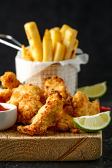 Buttermilk chicken nuggets served on wooden board with potato chips, lime wedges and tomato ketchup