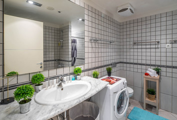 Interior of bathroom with grey tile on the walls and floor. Washing machine. Sink and mirror.
