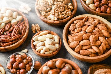 A variety of nuts in wooden bowls from top view. Walnuts, cashew, almond, pistachio, pecan, hazelnut, macadamia and peanut mix selection. Healthy fitness super food.