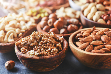 Mix nuts in wooden bowls on dark stone table. Almonds, pistachio, walnuts, cashew, hazelnut.