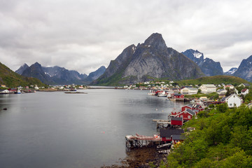 Fototapeta na wymiar The city of Reine in Lofoten/Norway. Long exposure shot with overcast scenery. The famous Mount Olstind and snow covered mountains in the background. Traveling and Norwegian concept.