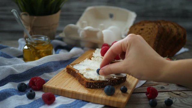 Female hands making a sandwich. Putting blueberries on bread. Close-up.