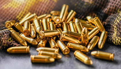 Pile of fire bullets or ammunition on dark stone table.  Hand guns weapon in background. Many projectiles into 9mm gun. - obrazy, fototapety, plakaty
