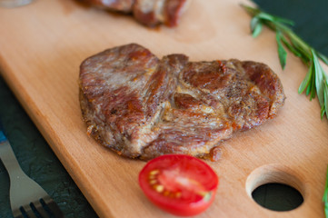 Grilled veal, beef or pork steak, tomato, rosemary and soy sauce for meat, knife and fork, on a wooden board, close-up