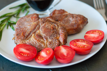 Fragrant pork meat steaks with spices, tomatoes and sauce, on a gray plate, on a dark concrete background, close-up